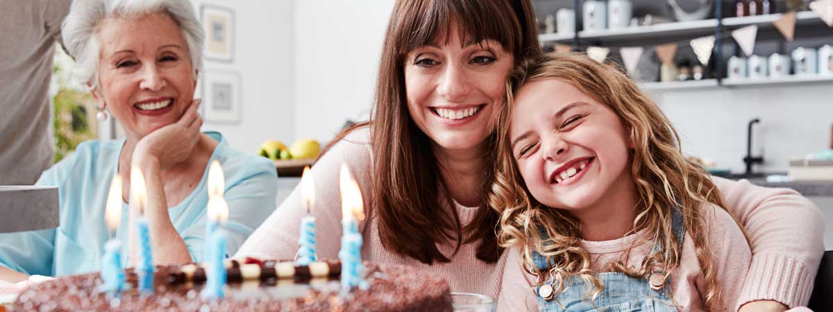 Drei Generationen - Oma, Mutter und Tochter - freuen sich darüber, ihre Küche mit KüchenTreff Willmes finanziert zu haben und blasen am Geburtstagstisch die Kerzen auf der Geburtstagstorte aus.