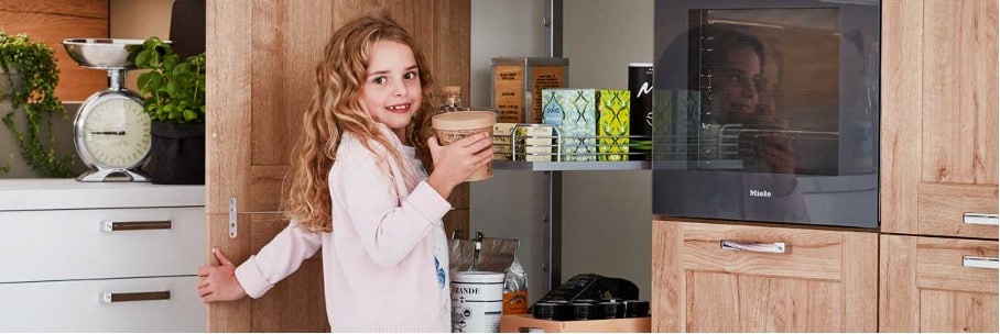 Mädchen mit blonden Locken holt sich einen Pappbehälter mit Müsli aus dem Apothekerschrank in einer modernisierten Küche von KüchenTreff Willmes.
